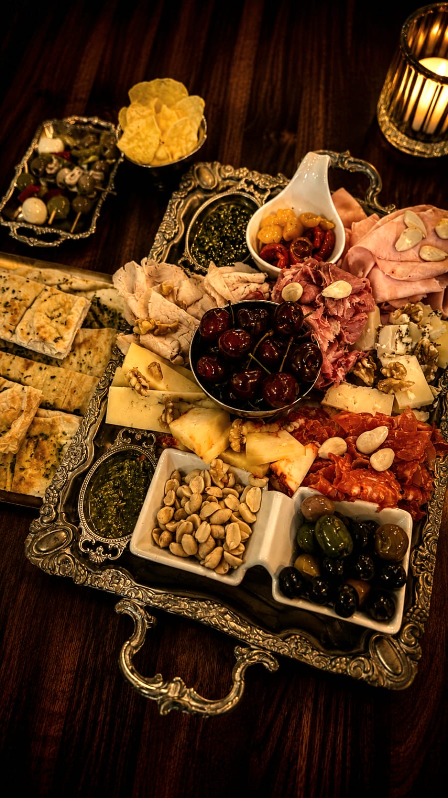 Tabla grande de plata con embutidos, quesos, cerezas, pesto y focaccia a la luz de las velas