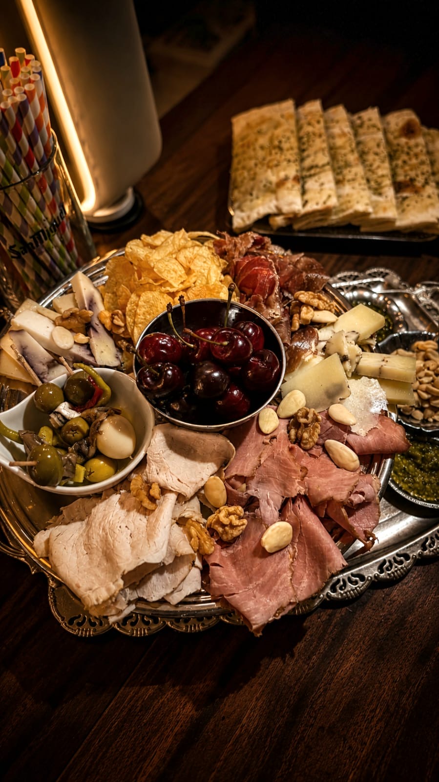 Tabla redonda con jamón, pavo, quesos curados, cerezas y aceitunas junto a focaccia